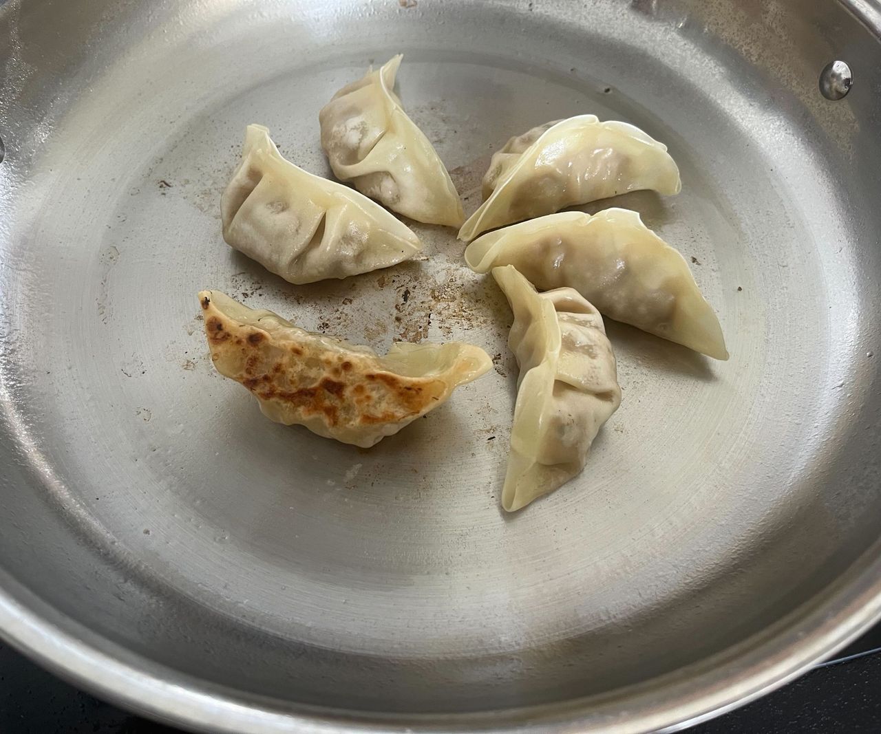 Gyoza dumplings being fried in a stainless steel frying pan, one on its side to show a crispy base.