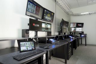 Each camera and microphone throughout the building ties back via NAV to the operator stations within the DE control room. This enables remote monitoring, audio mixing, and control.