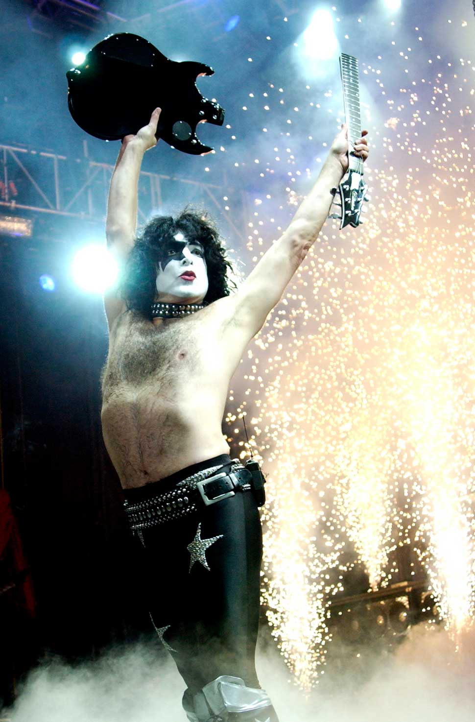 Paul Stanley holding a smashed guitar above his head onstage