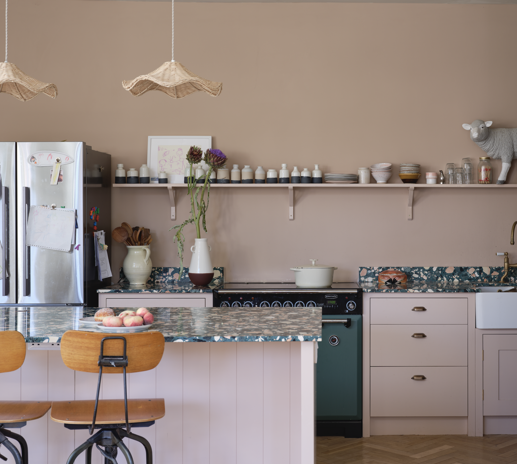 A kitchen painted a dusty pink with terrazzo counters and wavy rattan lighting pendants