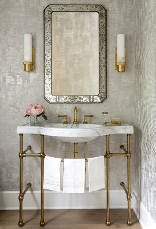 traditional bathroom with marble and brass vanity, wooden floors, wallights, vintage mirror