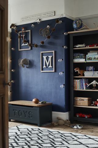 boy's bedroom with dark blue wall, bookshelf, toy chest, bulb lights, globe, rug