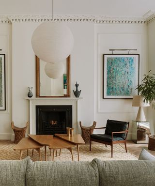 A white living room with a green sofa, layered coffee table, and white lantern-shaped pendant