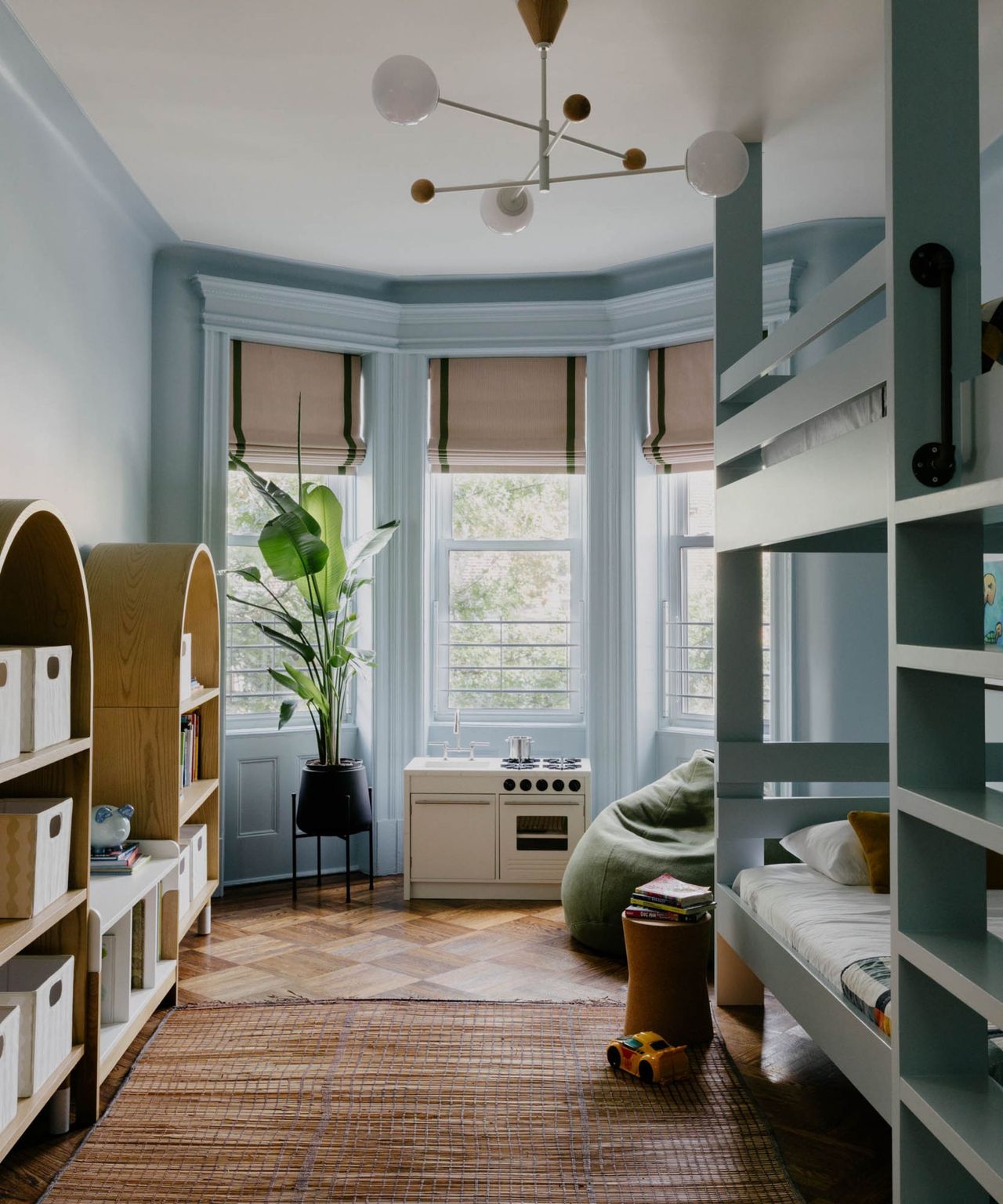 A light blue brownstone kids' bedroom with bunkbeds, three windows and wooden shelving