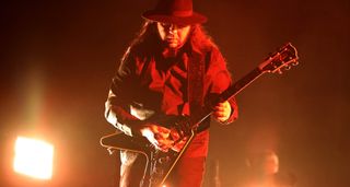 Daron Malakian of System of a Down performs live in a wide-brimmed had with a custom Flying V with an open-book Gibson headstock.