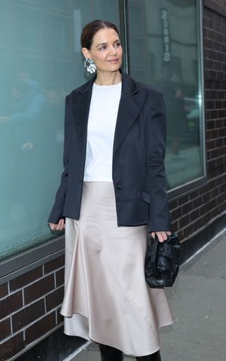 A photo of Katie Holmes accessorizing her outfit with a black woven leather clutch and textual silver statement earrings.