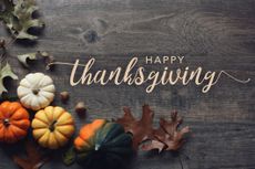 Gourds and tree leaves scattered on a wood table with the words "Happy Thanksgiving"