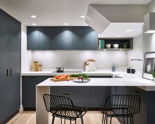 An example of modern kitchen lighting ideas showing a white kitchen with dark blue cabinets and black bar stools