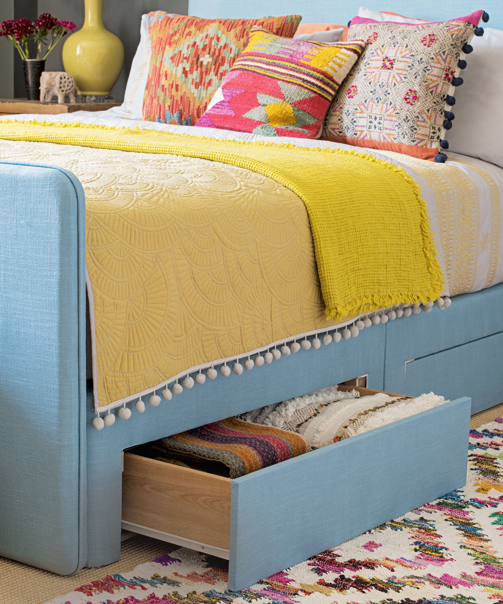 Blue upholstered bed with colourful cushions and under bed storage drawer