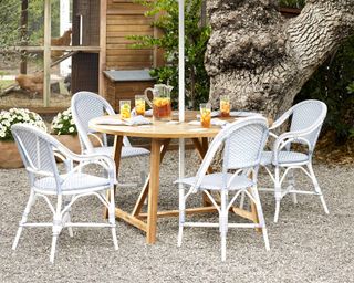 A circular wooden garden table surrounded by rattan-effect outdoor dining chairs