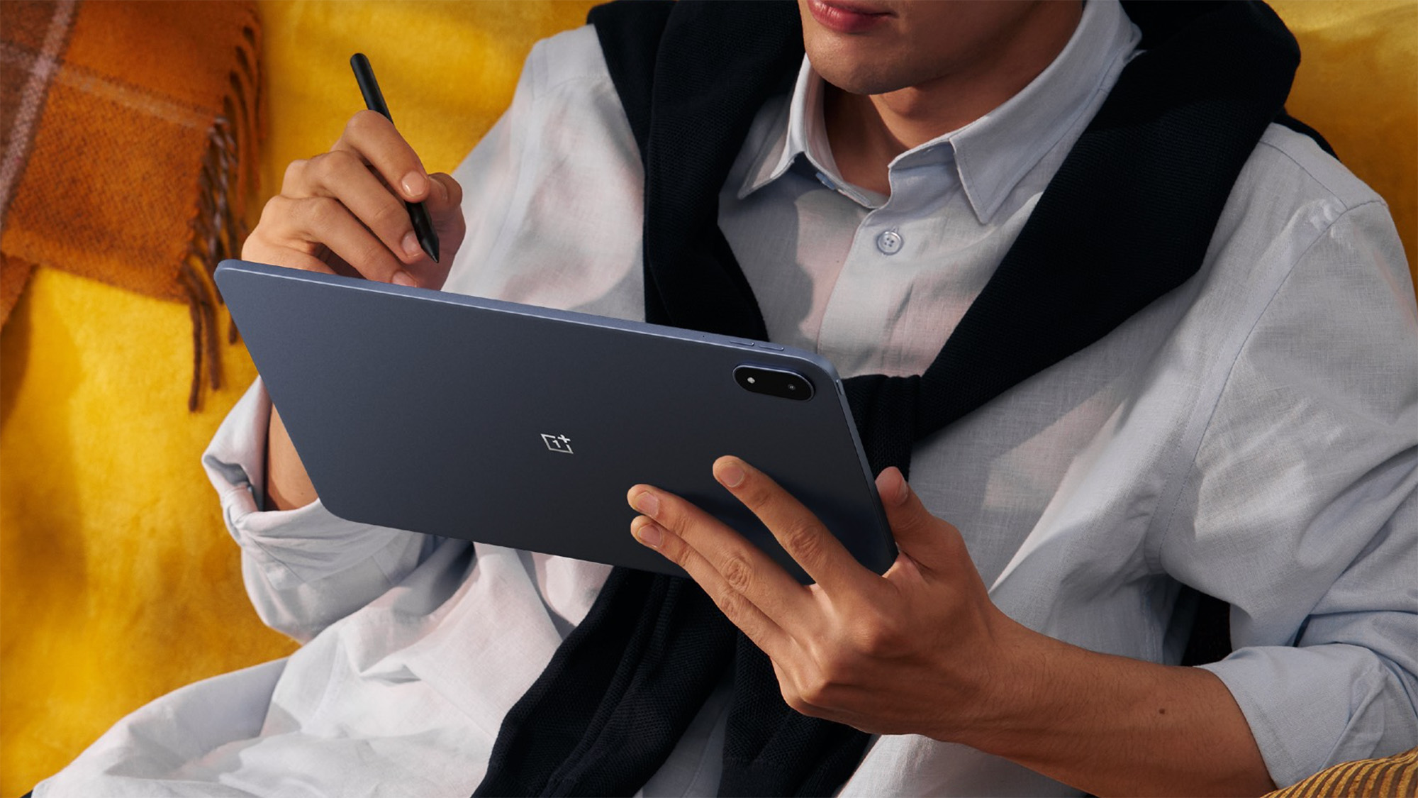 OnePlus Pad 3 lifestyle image of person sitting on yellow couch and using tablet and OnePlus Stylo 2