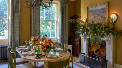 Yellow dining room decorated for Christmas with a wooden table and green chairs and green curtains at the window