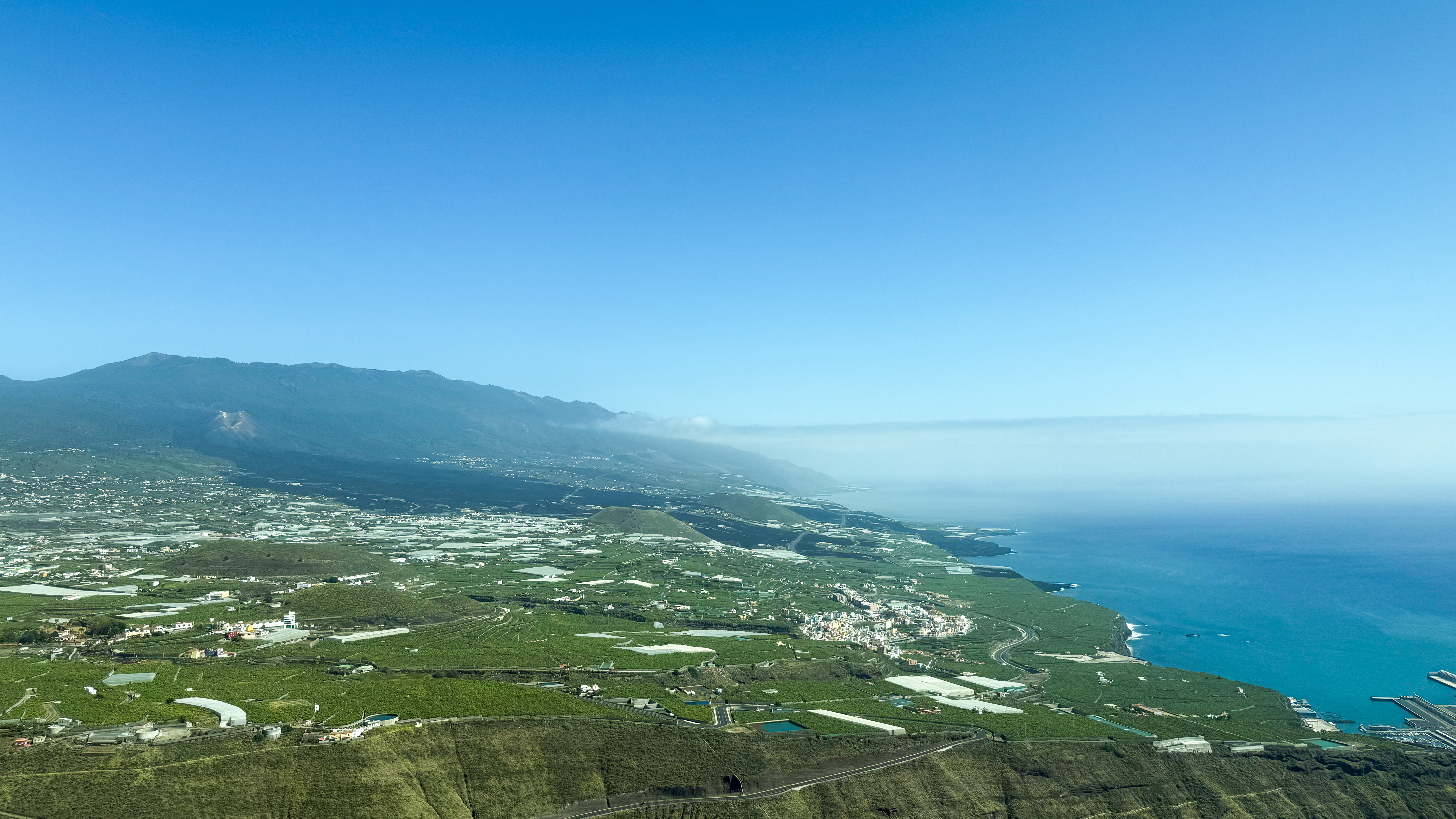 a distant view of a volcano and a large black lava field, which is now rock. You can see where it once flowed from the volcano all the way to the sea.