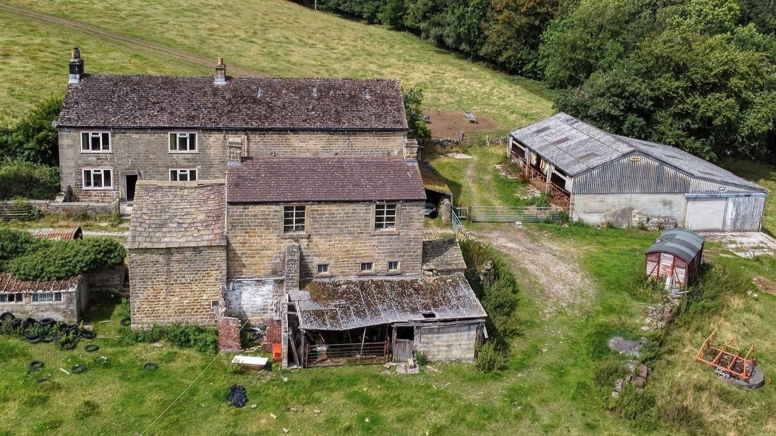 A stone farmhouse with adjourning buildings built on a sloped site