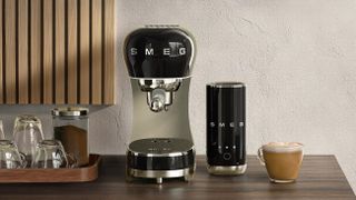 Smeg coffee maker and milk frother on wooden table with coffee and glass cups