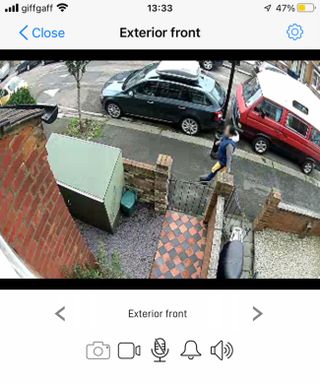 the street view from a security camera, showing a woman walking past a house and cars parked in the background