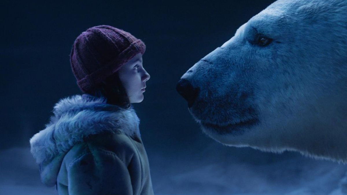 A girl stands opposite a polar bear wearing a beanie 