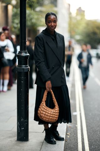 woman wearing a double-breasted blazer, a pleated midi skirt, and lace-up lug sole boots