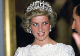 Princess Diana wearing a pearl and diamond tiara and a white lace dress smiling and looking to the side