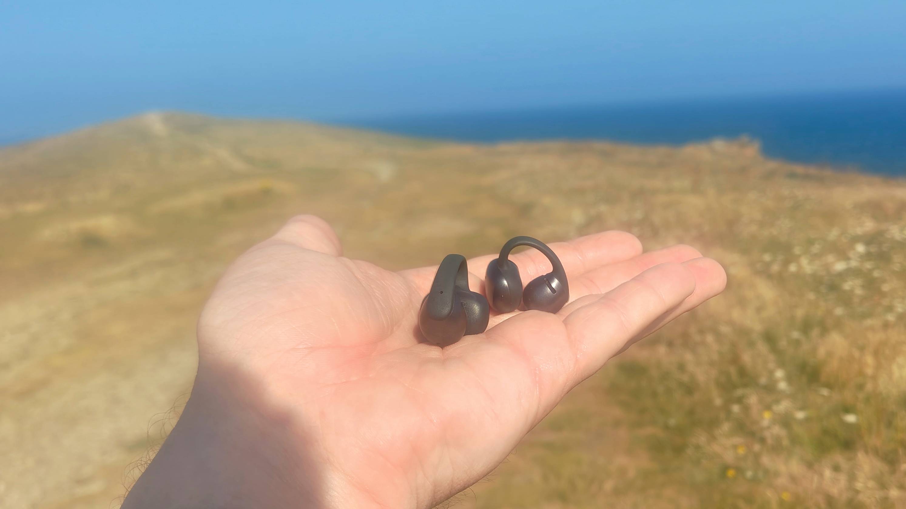 The Shokz OpenDots One in a man's hand near the sea.