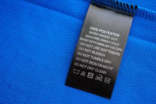 A black washing label with how to wash is shown attached to a blue garment