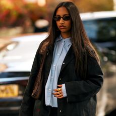 A woman in London wears a blue button-up green jacket and brown bag.