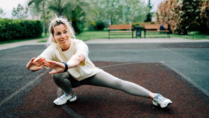 Woman smiling while performing a hip and groin stretch in side lunge outdoors in park