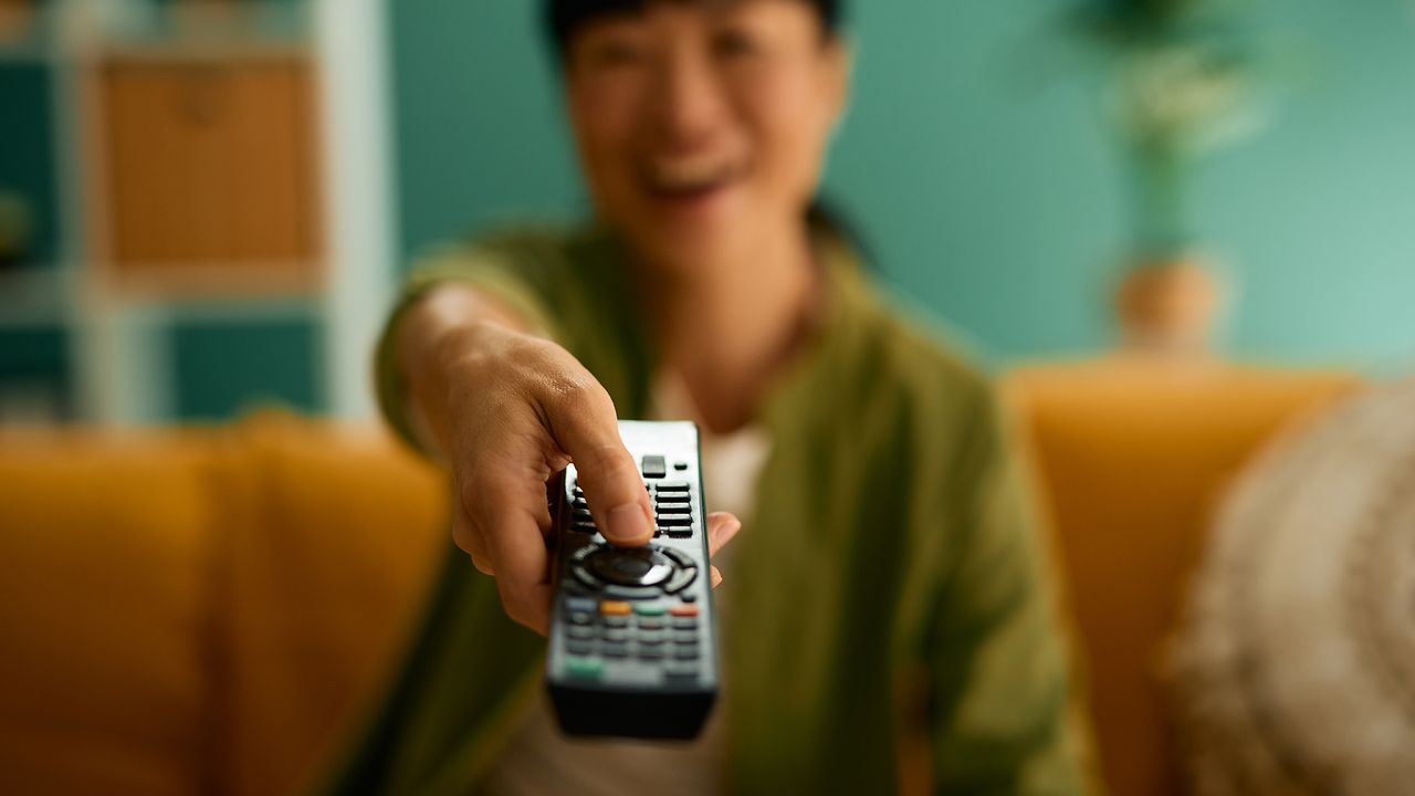 Woman pointing remote control out of the screen