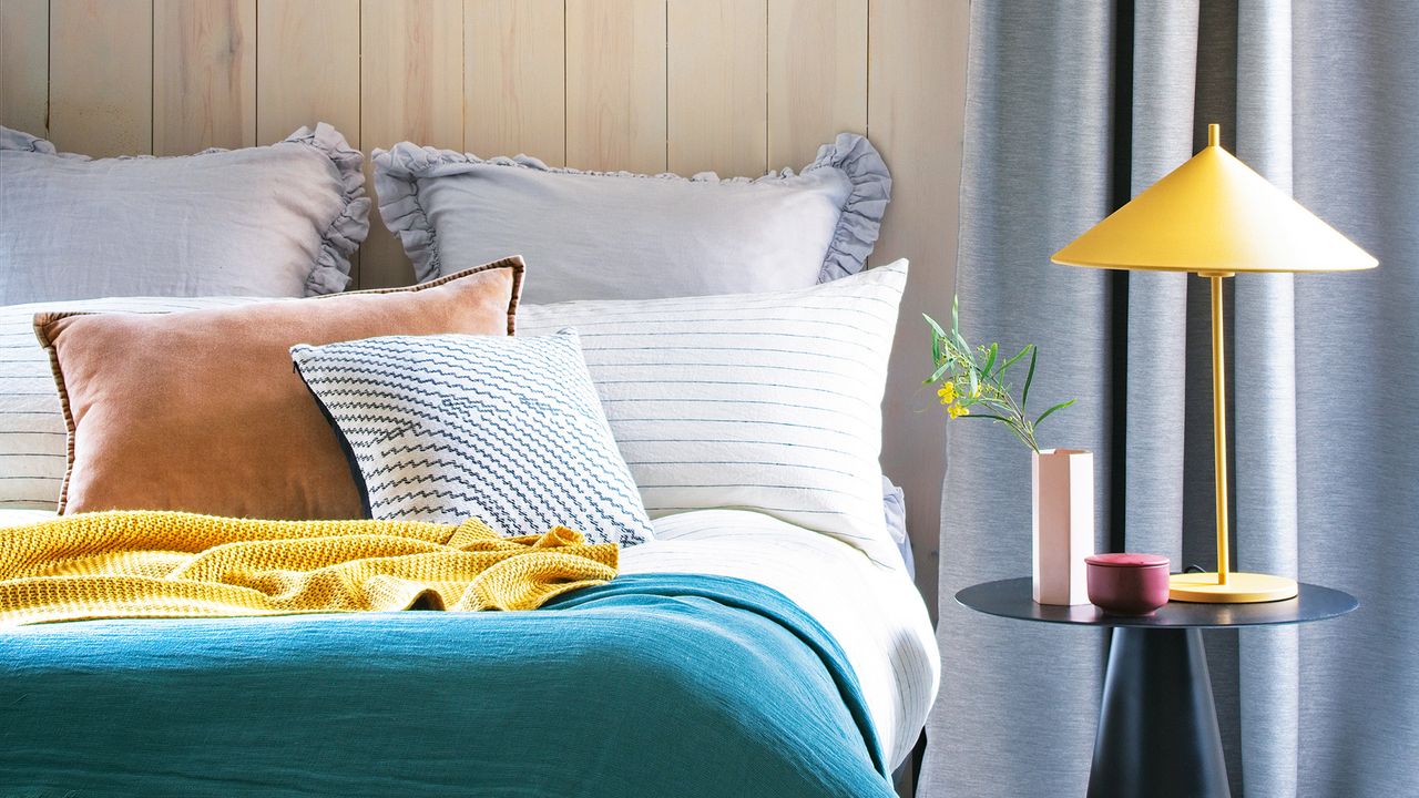 A bed with multiple pillows and cushions and a teal throw