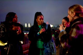 a group of women stand on a nighttime rooftop while holding small bottles, in 'Queenie'