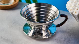 kalita wave stainless steel pour-over coffee dripper photographed against a blue background with kalita filters