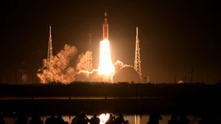 rocket launch with bright orange engine flames as it soars into the dark sky. 
