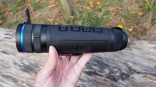 Pulsar Telos XQ35 monocular held in a hand outside in front of a log