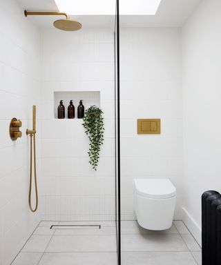 All white bathroom with white wall and floor tiles and brass shower hardware