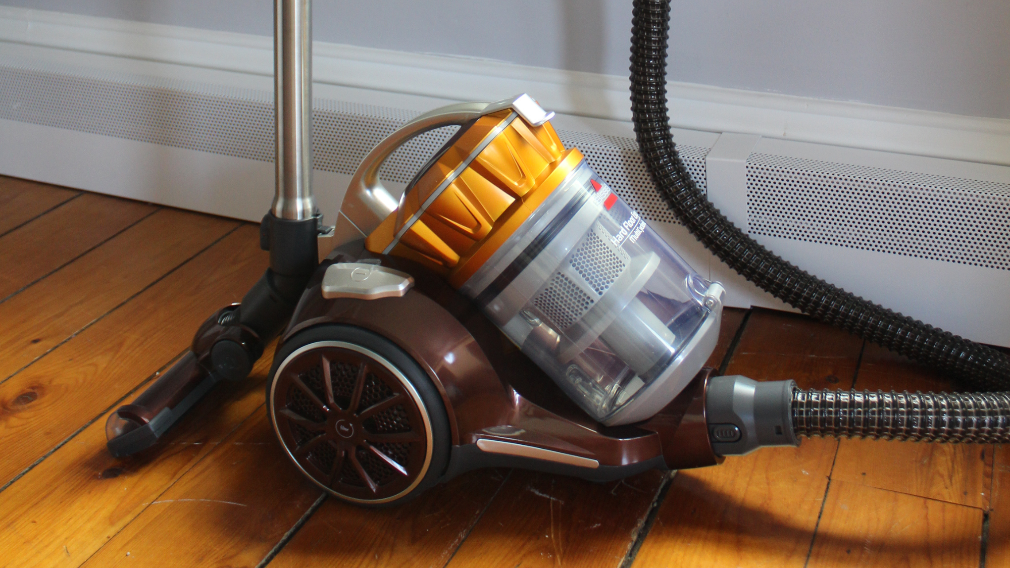 Bissell Hard Floor Expert canister vacuum cleaner on wooden floor in front of white wall.
