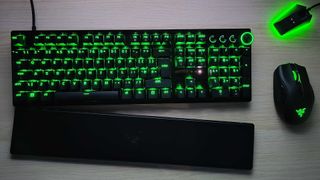 A Razer Huntsman V3 Pro seen top-down on a wooden surface alongside a mouse and mouse dock, with the wrist rest slightly apart