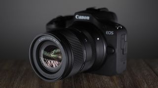 The Sigma 18-50mm f/2.8 DC DN | C Canon RF lens, mounted to a Canon EOS R100, on a wooden surface against a dark background with moody lighting