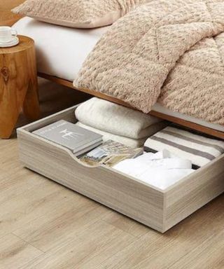 An image of a bed with a wooden storage drawer sticking out from underneath it
