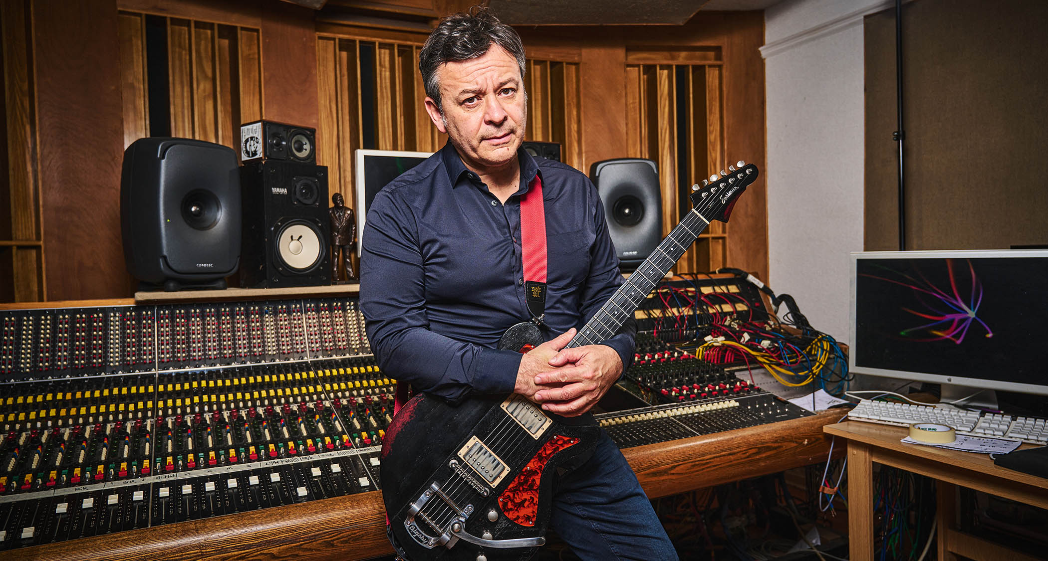 James Dean Bradfield of the Manic Street Preachers pictured in the studio where he showed guitarist his Eastman and Gordon Smith guitars. He wears a dark blue shirt, studio hardware occupies the background.