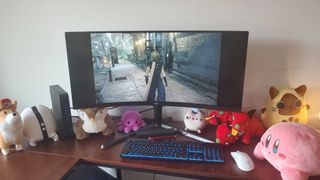 a large curved monitor on a wooden desk with several plushies under it