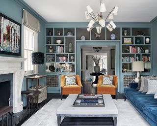 Formal living room ideas with blue walls, built-in bookcases, blue velvet sofa and orange velvet armchairs