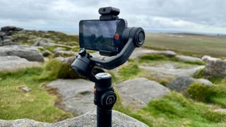 Zhiyun Smooth 5S AI gimbal held in a hand outside in a green field