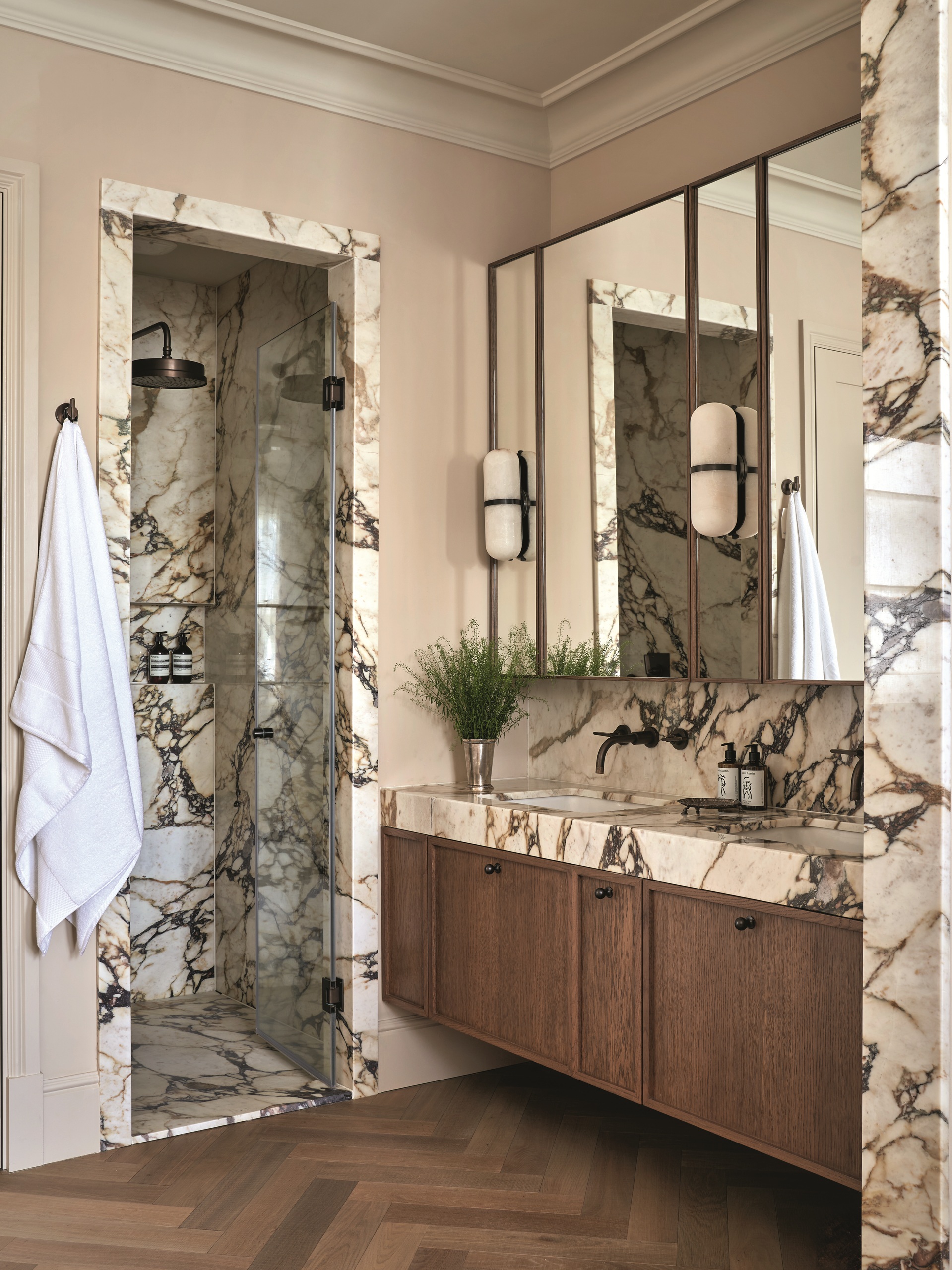 modern bathroom with plaster pink walls, marble walls and vanity and enclosed shower, with herringbone floor, timber vanity, and white towel