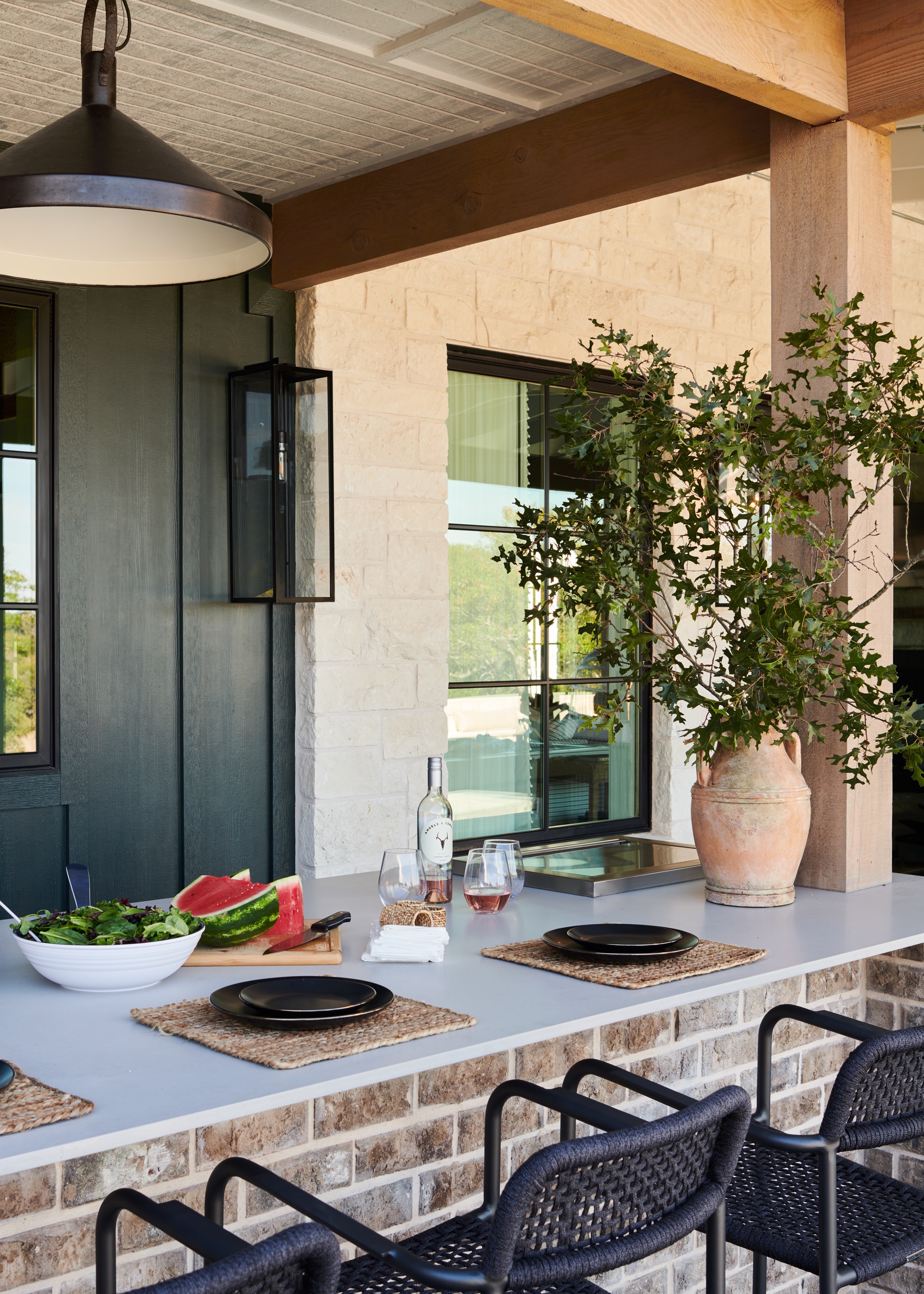 Outdoor kitchen bar with black stools and terracotta pot with oversized branches
