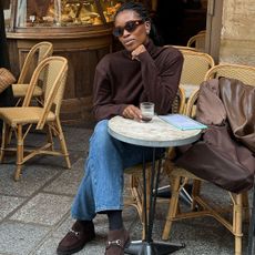 woman in brown turtleneck, jeans, and loafers at a cafe