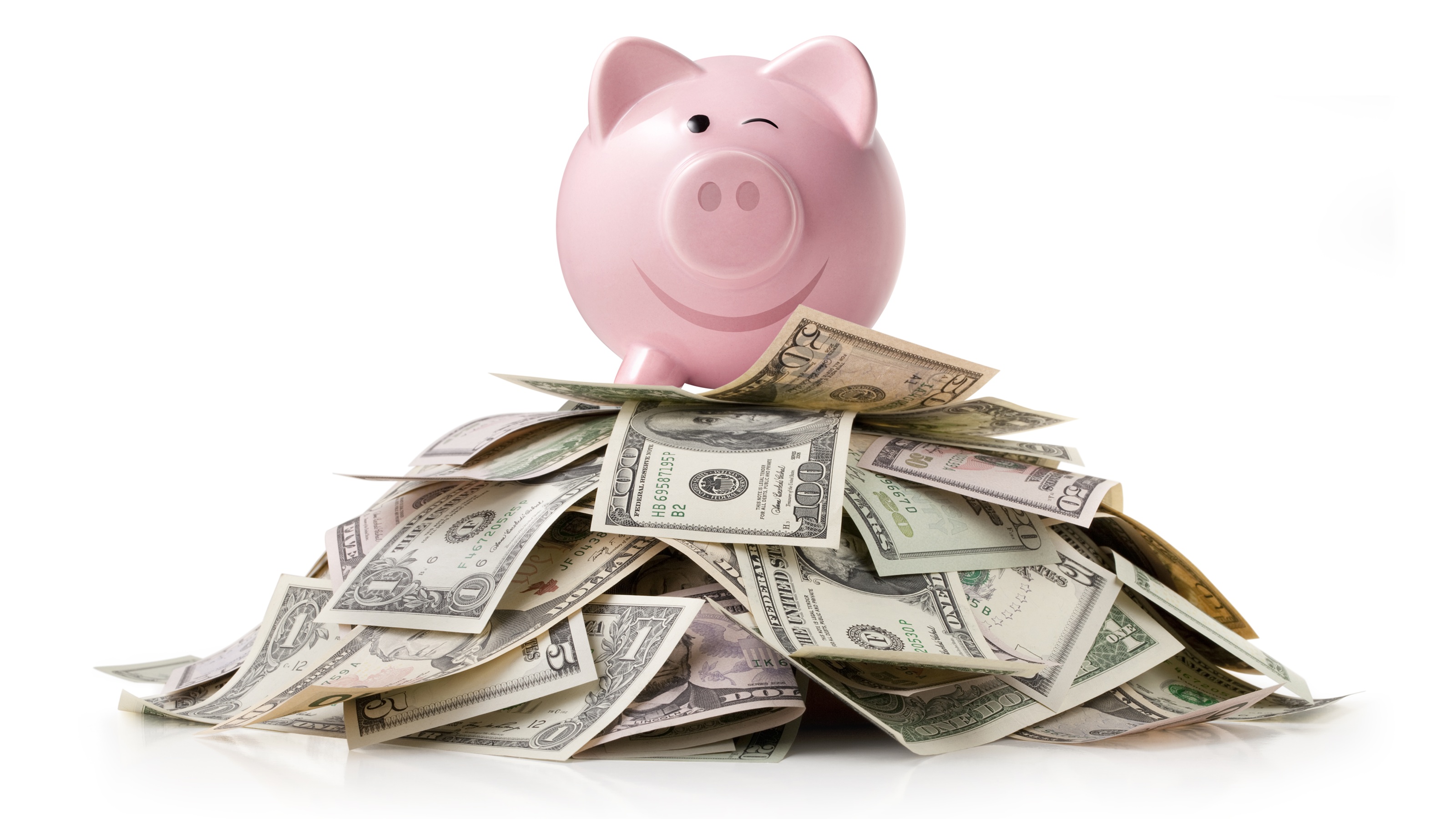 A winking piggy bank sits atop a pile of cash.