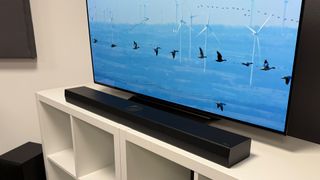 LG S70TY soundbar package on white shelving unit in front of TV showing birds in flight on screen