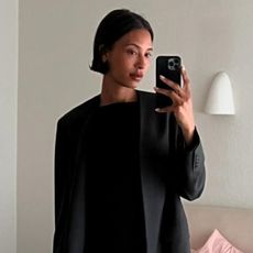 Woman wears black blazer and black mini dress while taking mirror selfie.