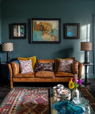 traditional living room with tan leather sofa and dark blue-green walls with will art