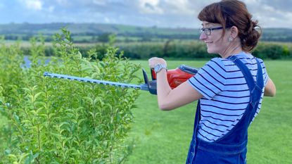 woman trimming a hedge with the Husqvarna 115iHD45 cordless hedge trimmer
